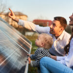 Mann zeigt Frau und Kind an einem warmen Tag die Sonnenkollektoren auf dem Grundstück in der Nähe des Hauses