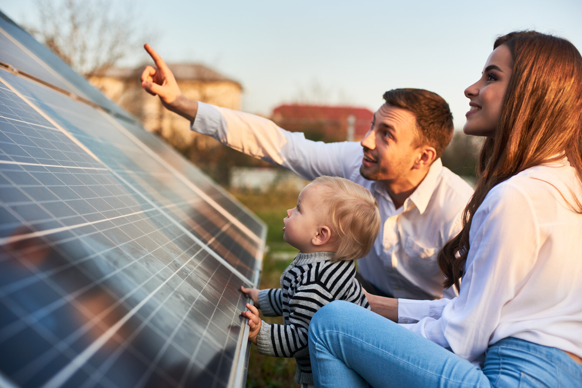 Mann zeigt Frau und Kind an einem warmen Tag die Sonnenkollektoren auf dem Grundstück in der Nähe des Hauses